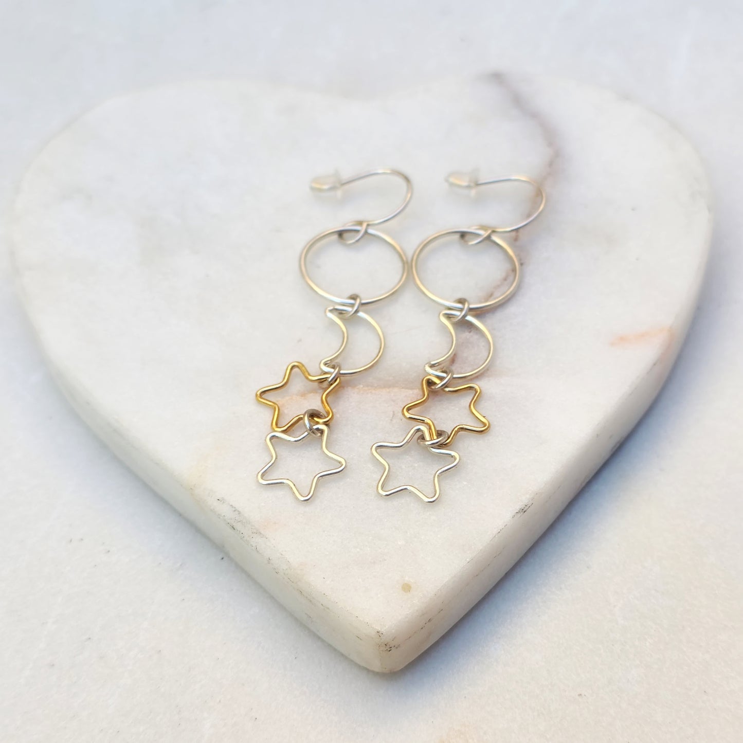 Dangle earrings with gold stars and silver moon charms on marble heart background