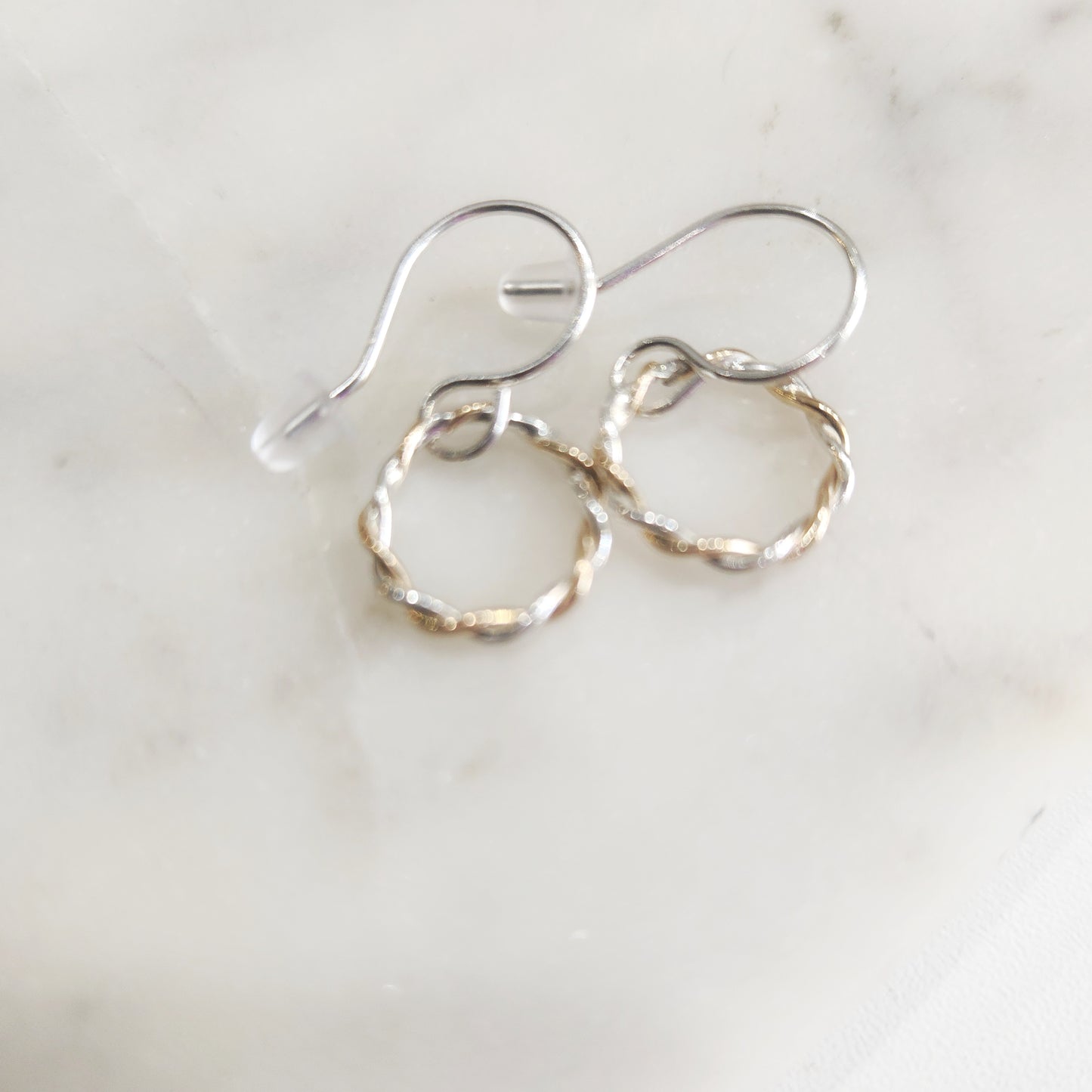 Minimalist hoop earrings made of twisted gold-filled and silver wire on marble background