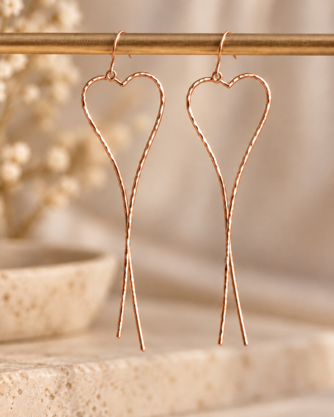Pair of rose gold-filled Allure Heart Earrings suspended against a soft neutral background, highlighting their warm rose-gold finish, hammered texture, and flowing heart design