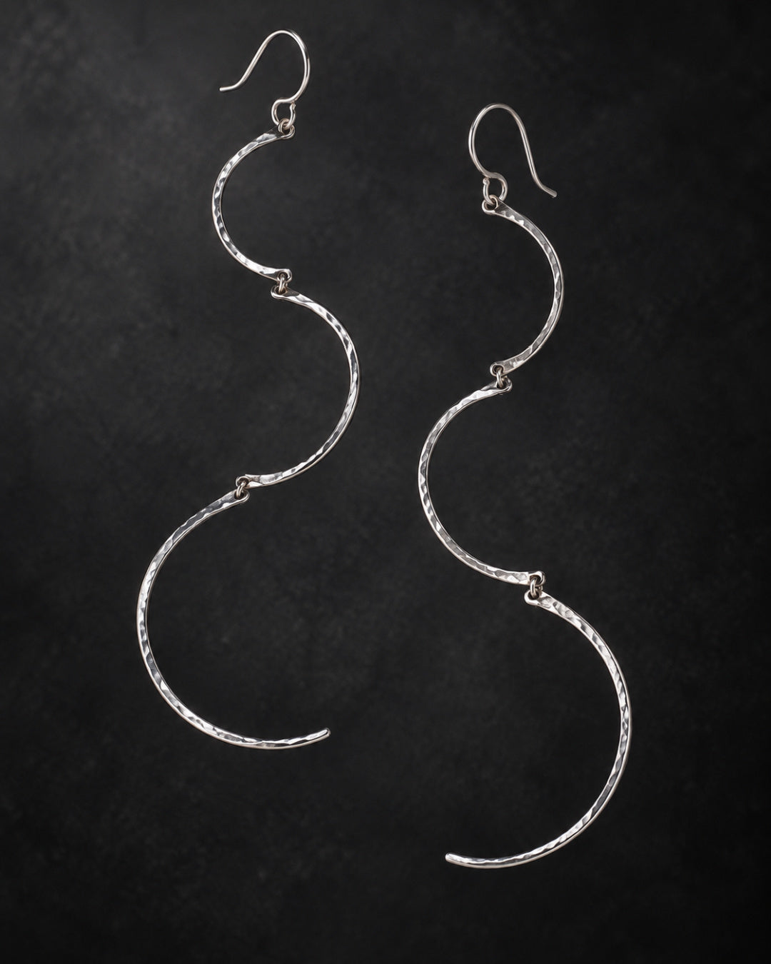 Suspended Cadence Earrings featuring three graduated, hand-hammered Argentium silver arcs against a charcoal-black background.