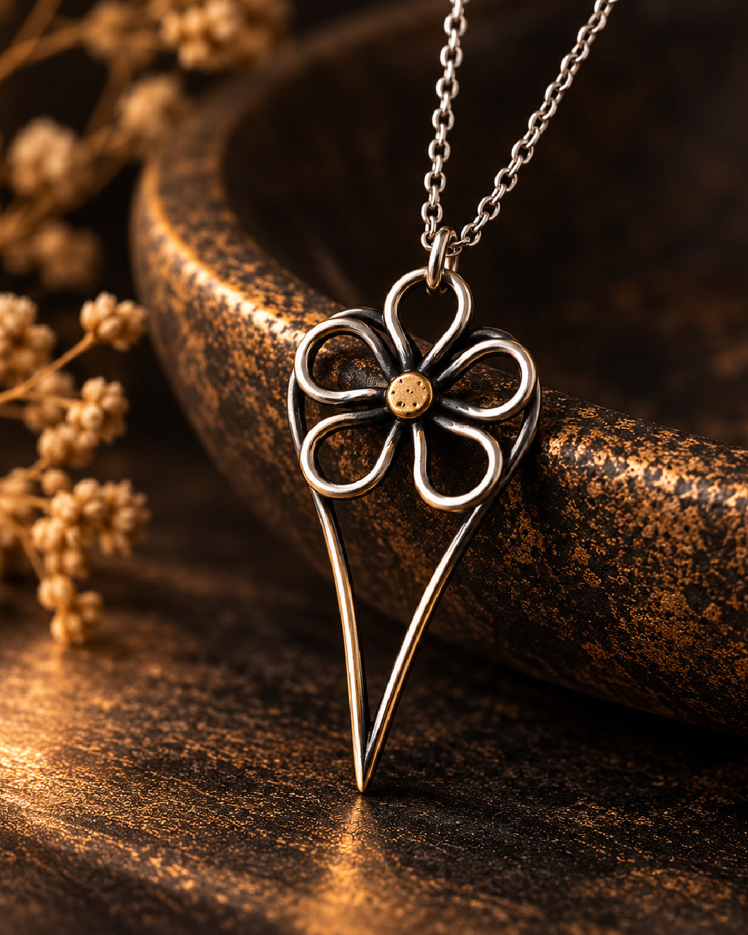 Wild Rose Heart Necklace photographed against a dramatic dark bronze setting, featuring sculptural silver petals, a warm gold center, and a long oxidized heart silhouette.