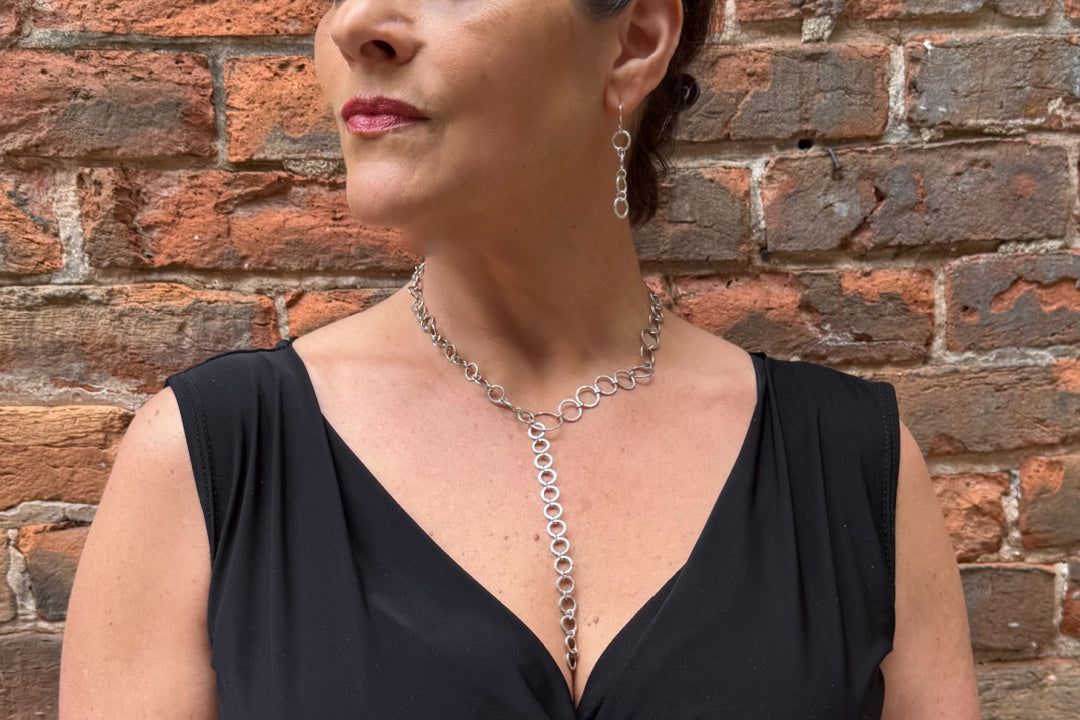 Woman wearing a black dress and silver necklace against a brick wall