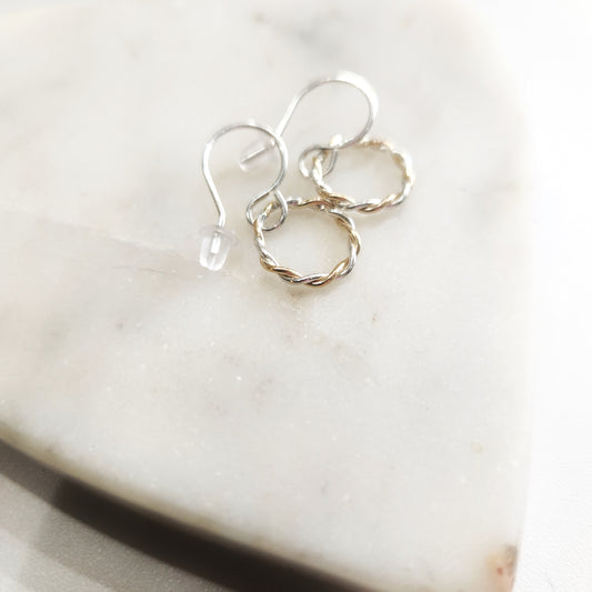 Tiny mixed metal hoop earrings displayed on white marble heart-shaped dish