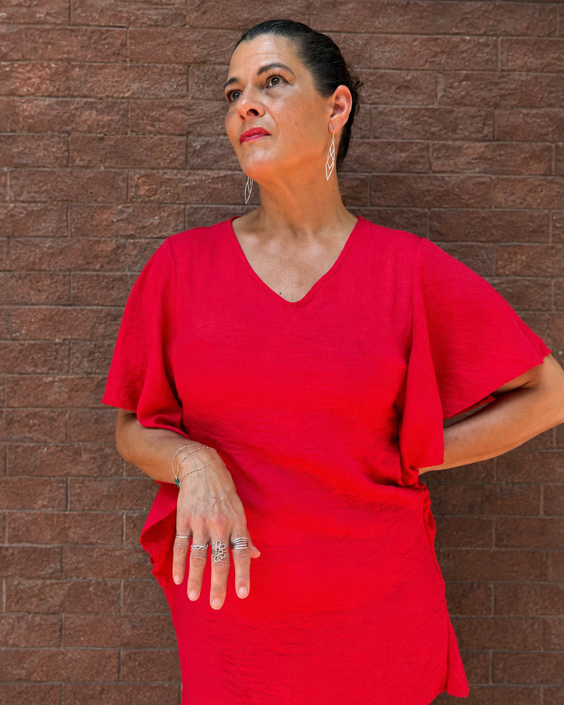 Kimberly Story wears the long sculptural River Dragon Earrings with a vivid red dress, posing confidently against a brick wall in Paducah, Kentucky.