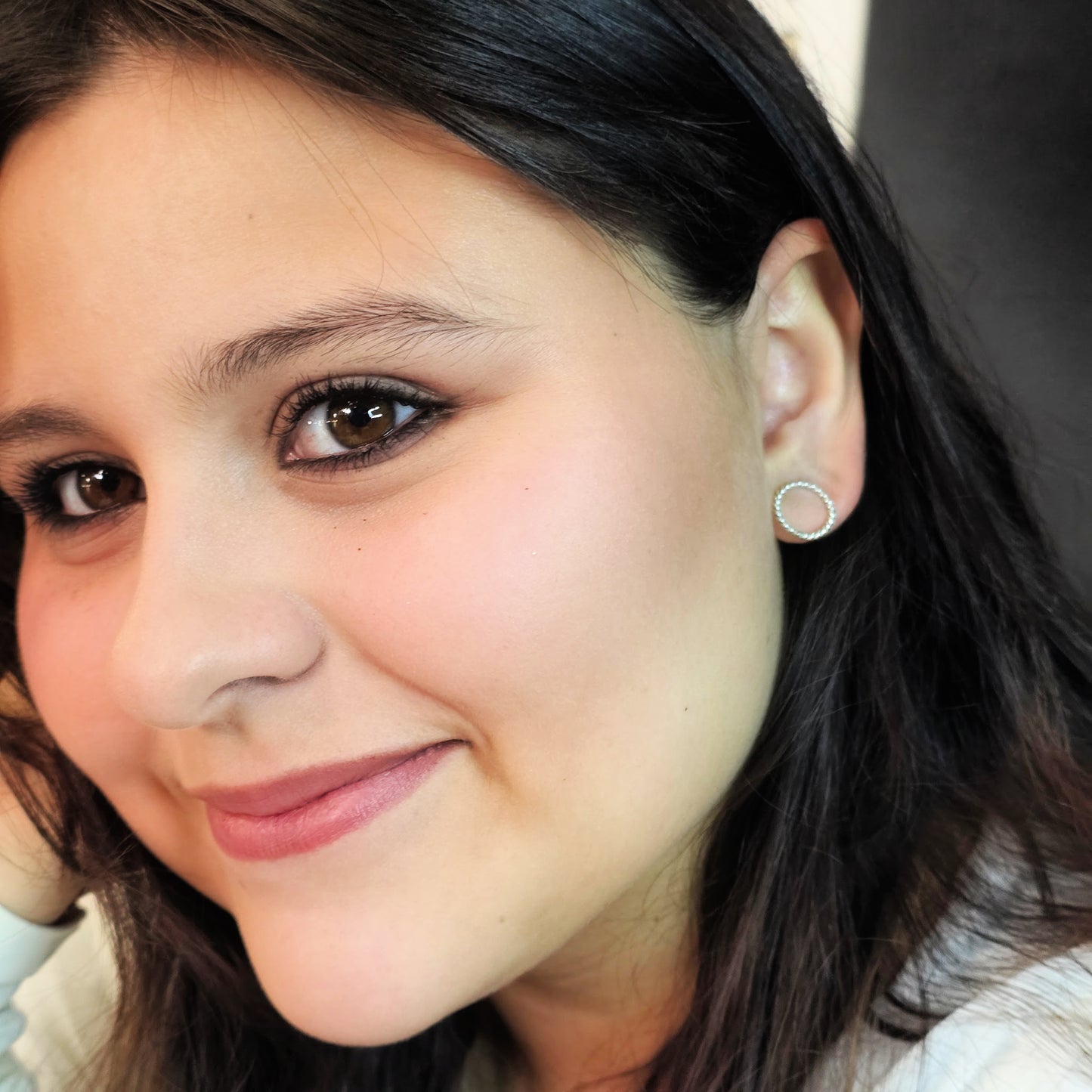Close-up of a woman with dark hair and earrings, wearing a light-colored top.