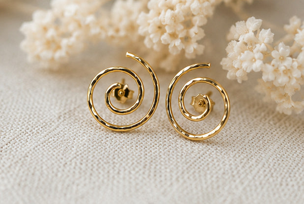 Gold spiral stud earrings styled with soft floral background, feminine modern jewelry