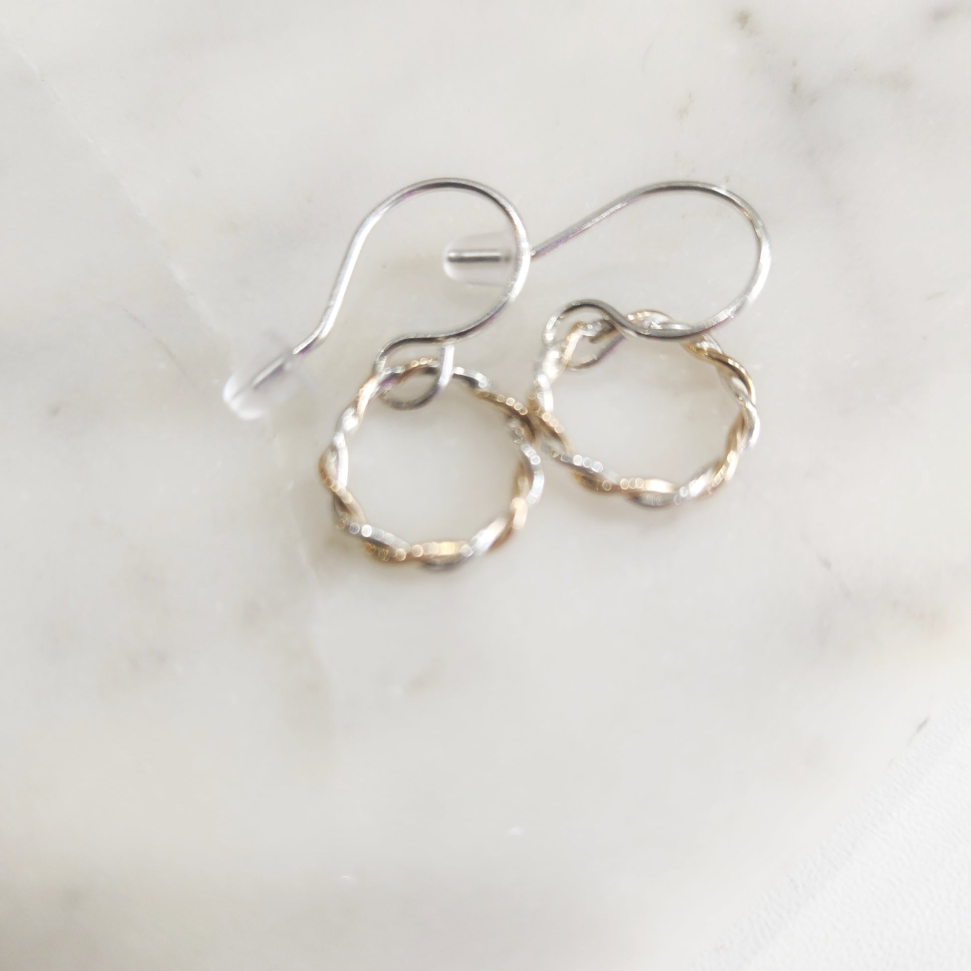 Minimalist hoop earrings made of twisted gold-filled and silver wire on marble background