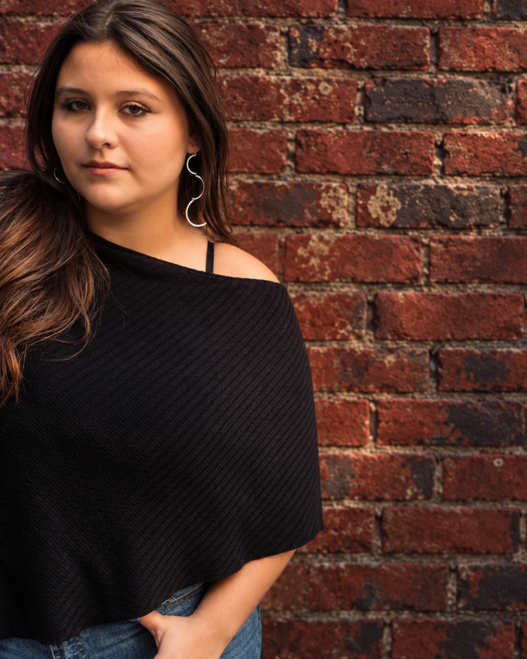 Woman wearing long sculptural Cadence Earrings in hammered Argentium silver against a weathered brick wall.