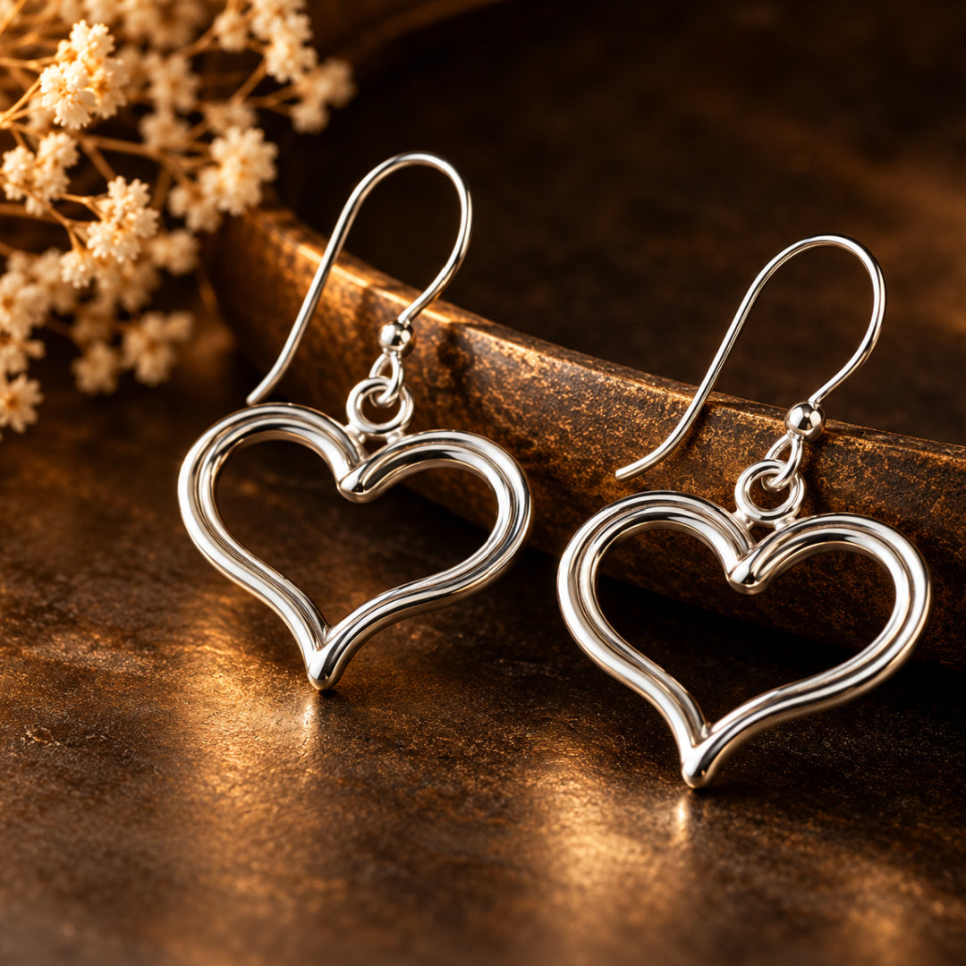 Devotion Heart Earrings by Lepa Jewelry photographed against a rich bronze background, showcasing polished silver heart silhouettes and elegant openwork design.