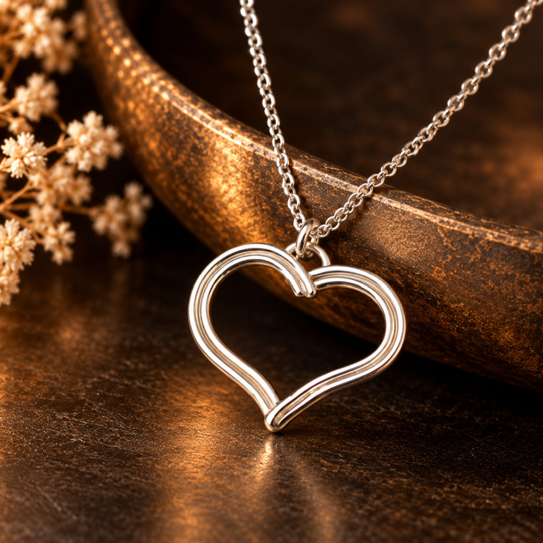 Devotion Heart Necklace by Lepa Jewelry photographed against a rich bronze background, showcasing the polished silver heart pendant, sculptural overlapping lines, and delicate chain.