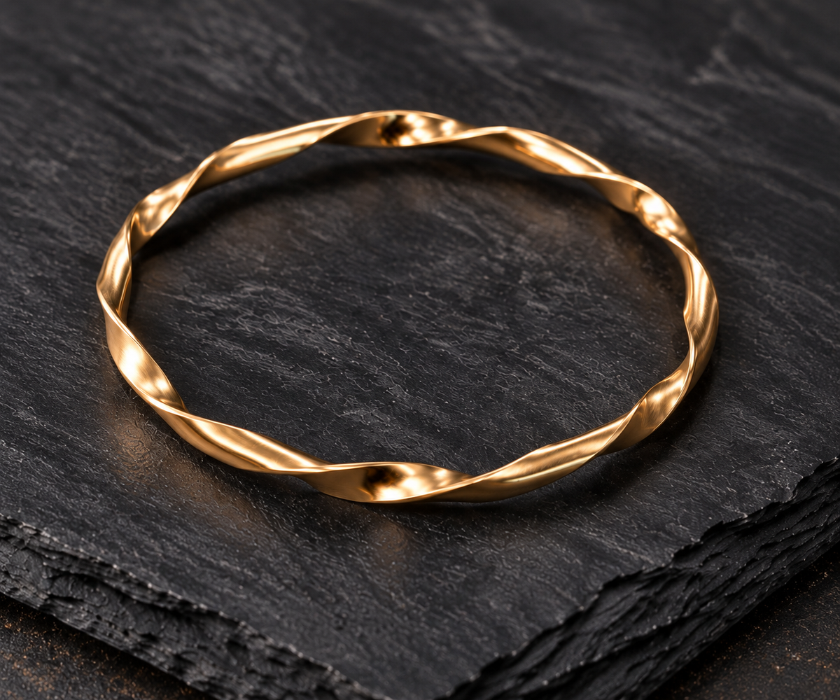A twisted gold bangle bracelet displayed on a textured black slate surface.