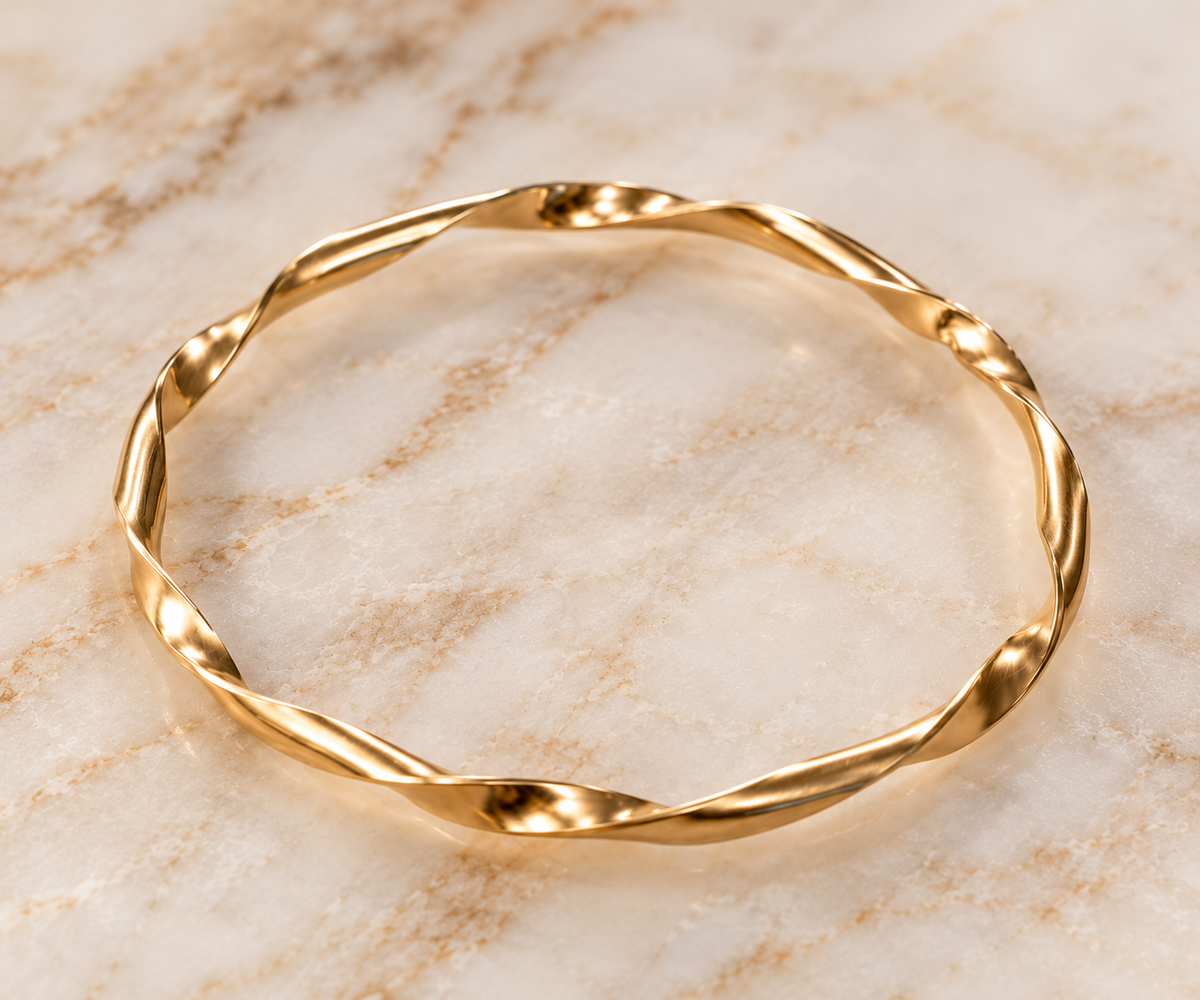 A structural gold bangle bracelet resting on a light beige marble surface.