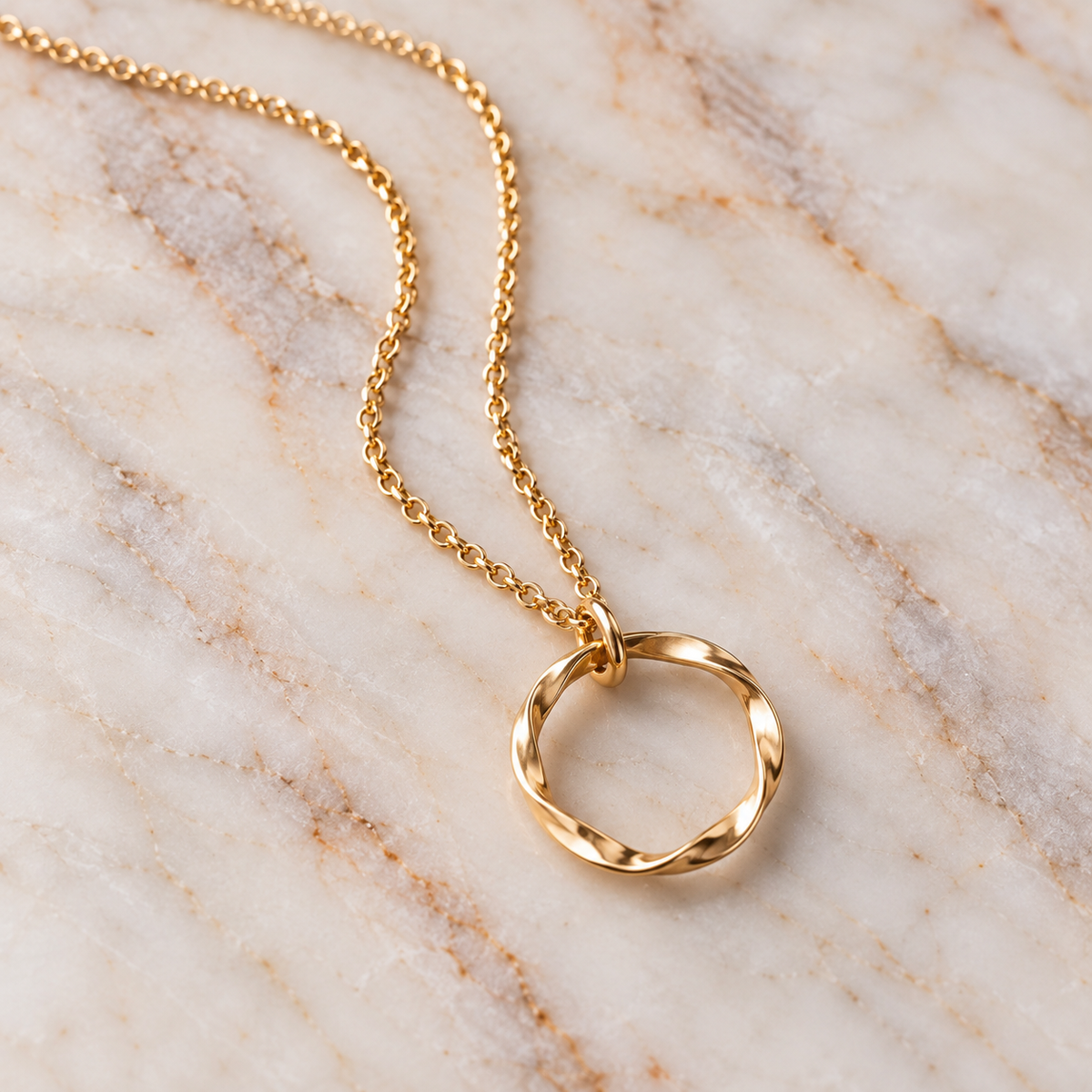 A gold chain necklace with a twisted open circle pendant, displayed on a light beige and white marble surface.