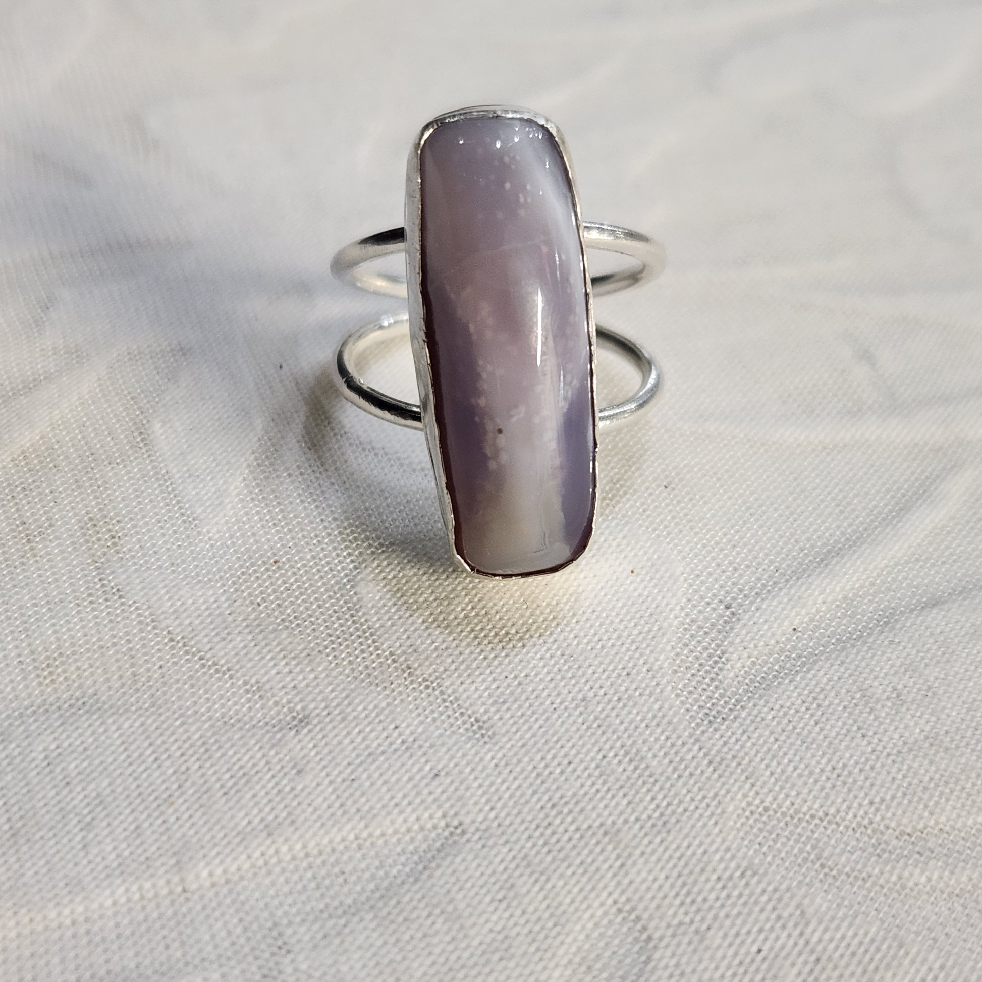 Flat lay image of lavender agate power ring with soft background, emphasizing its silver craftsmanship