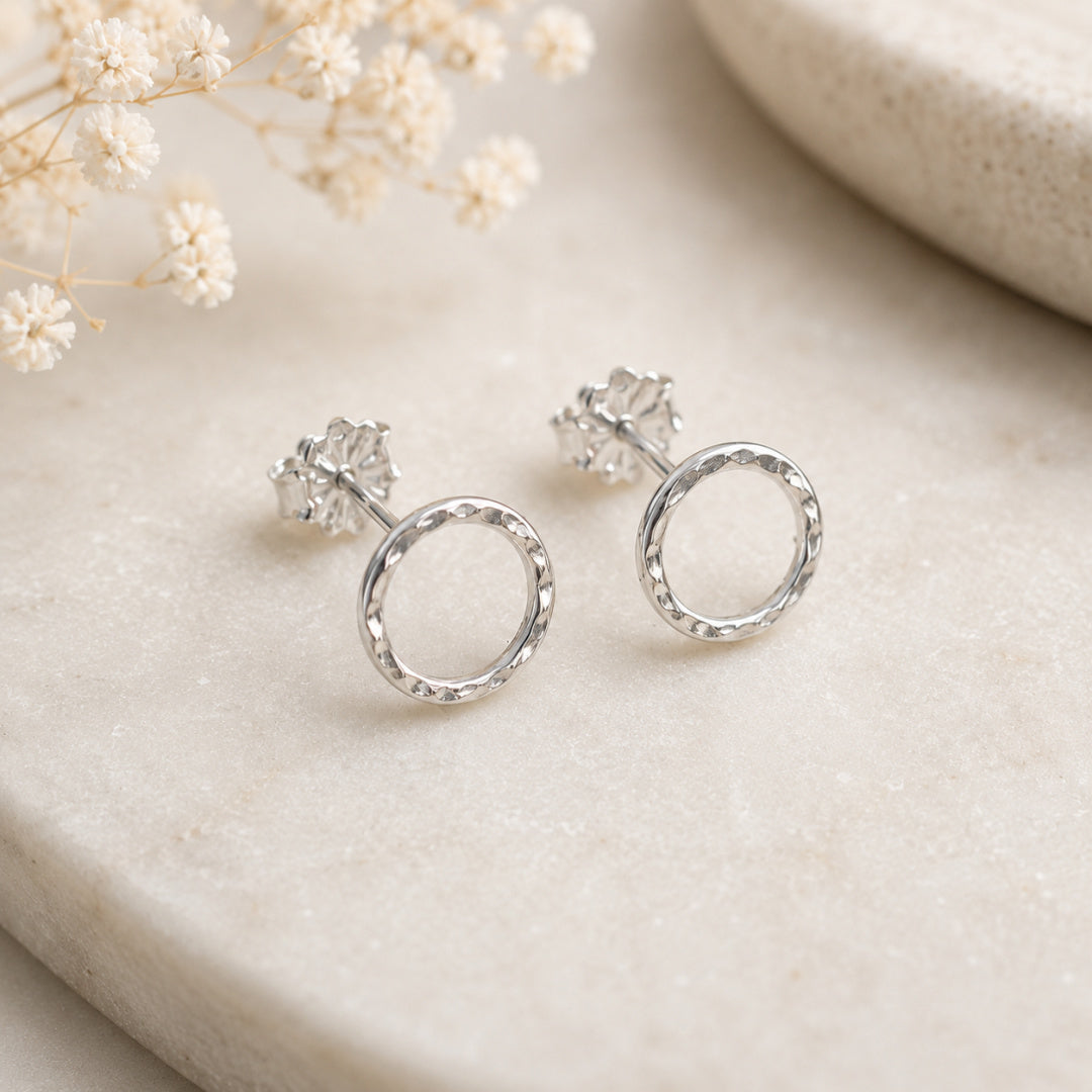 Side view of Argentium silver Karma Stud earrings with hammered texture displayed on marble with delicate floral styling