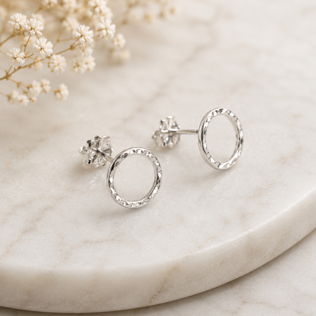 Angled view of Argentium silver Karma Stud earrings with hammered open circle design on neutral marble surface