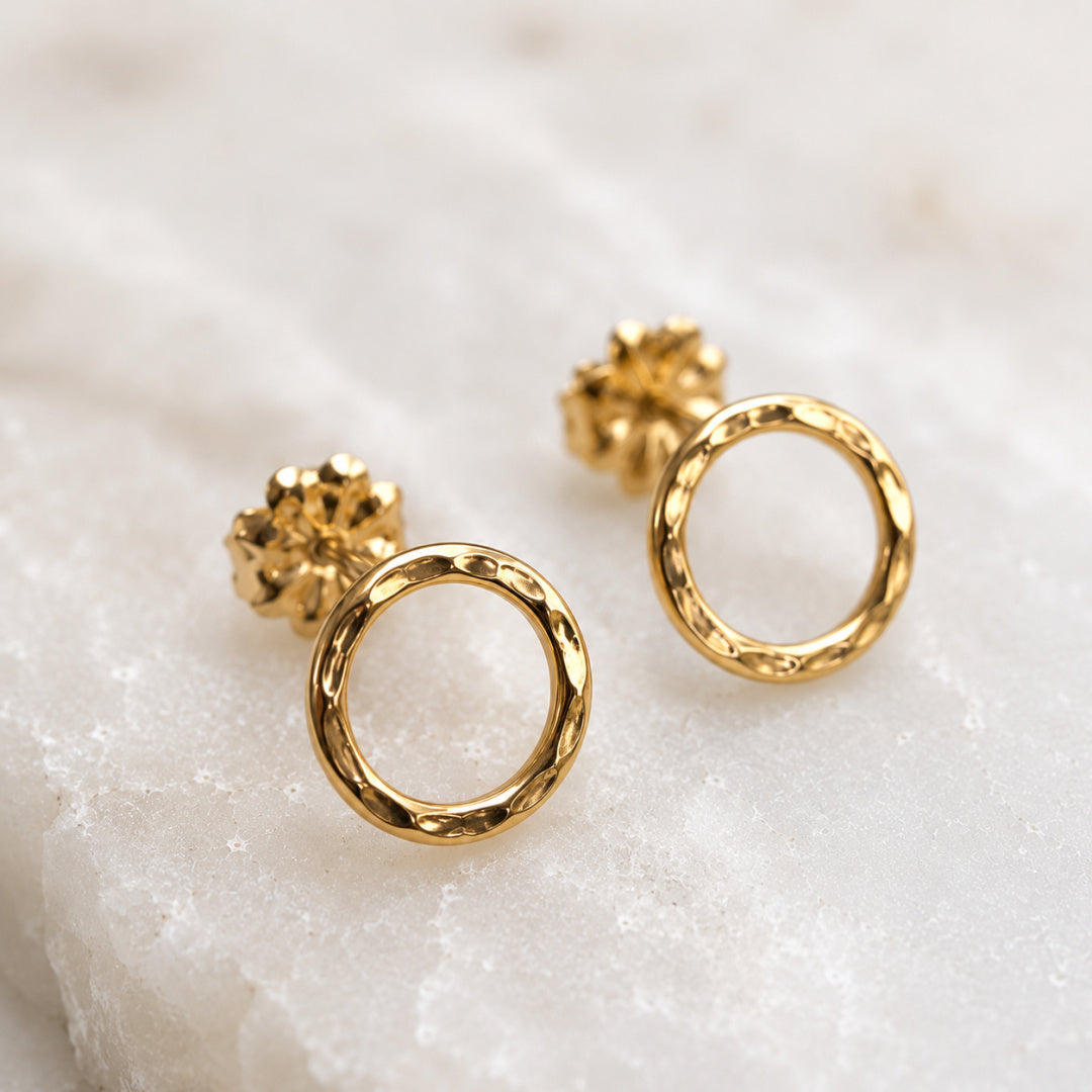 Close-up of gold-filled Karma Stud earrings with hammered texture and open circle design on neutral stone background