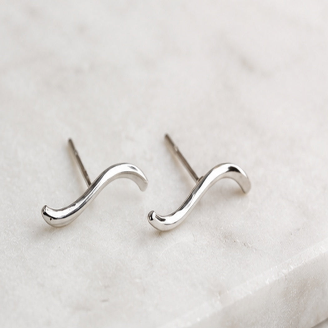 Sculptural silver wave stud earrings styled on a soft neutral surface, modern minimalist jewelry by Lepa Jewelry designed for effortless everyday wear