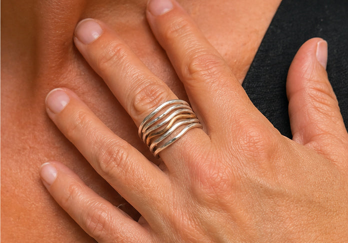 Close-up of the Lepa Wave Ring showing five flowing sterling silver strands with a single bronze wave accent. Modern mixed-metal stacked band design.

