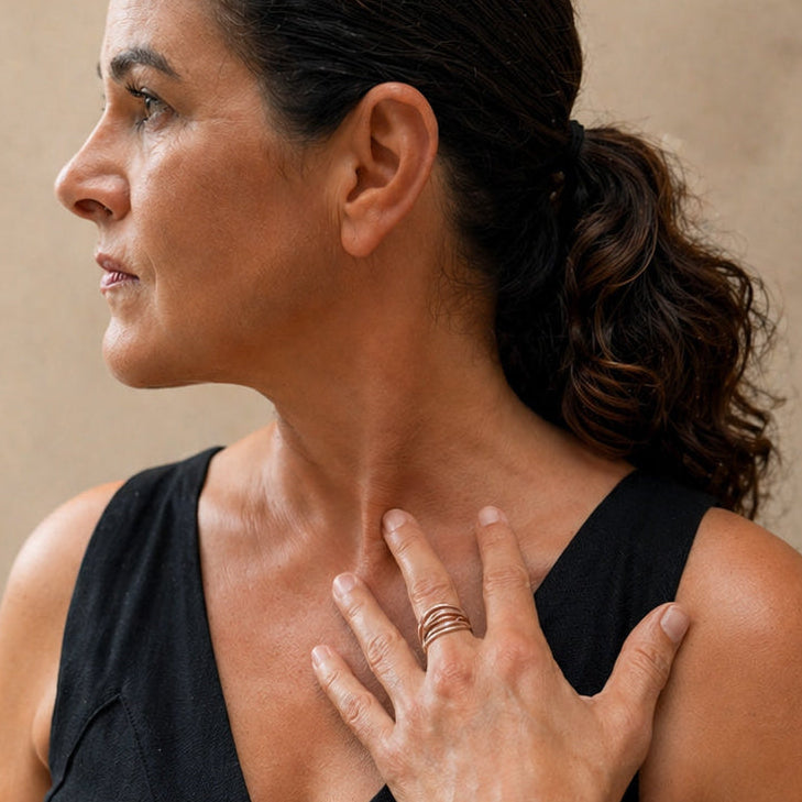 Woman's hand wearing the Lepa Wave Ring in sterling silver with bronze accent, resting on soft fabric. Five flowing bands create a sculptural stacked ring effect."
