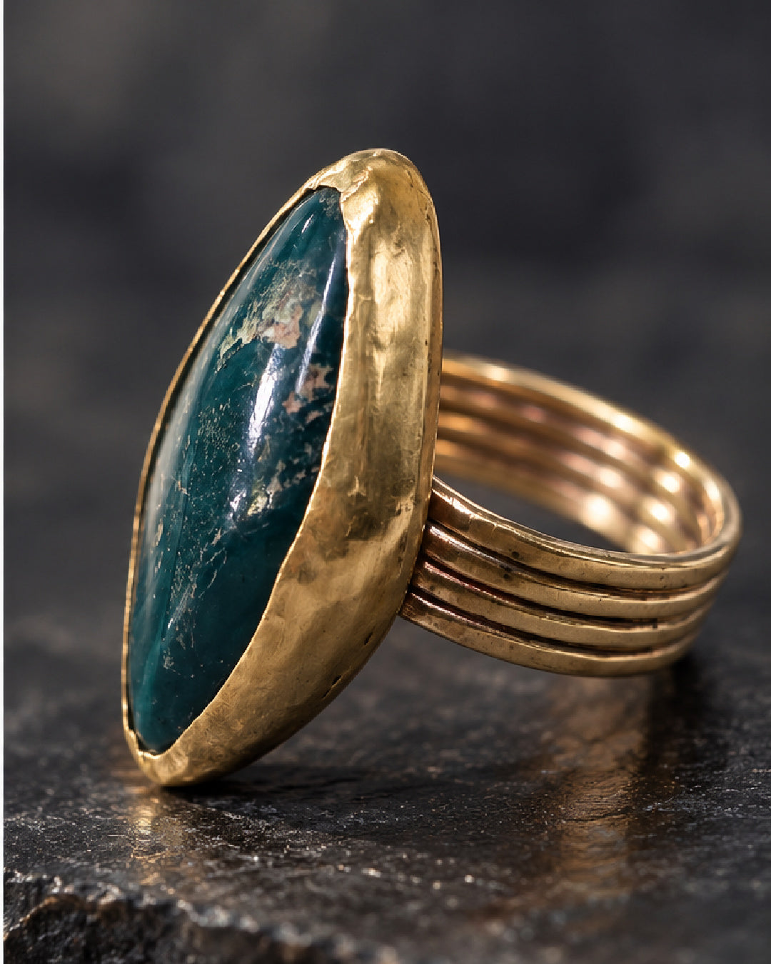 Side view of The Mariposa Ring by Lepa Jewelry, showing its deep green mariposite cabochon, substantial brass bezel, and architectural four-strand band against charcoal.