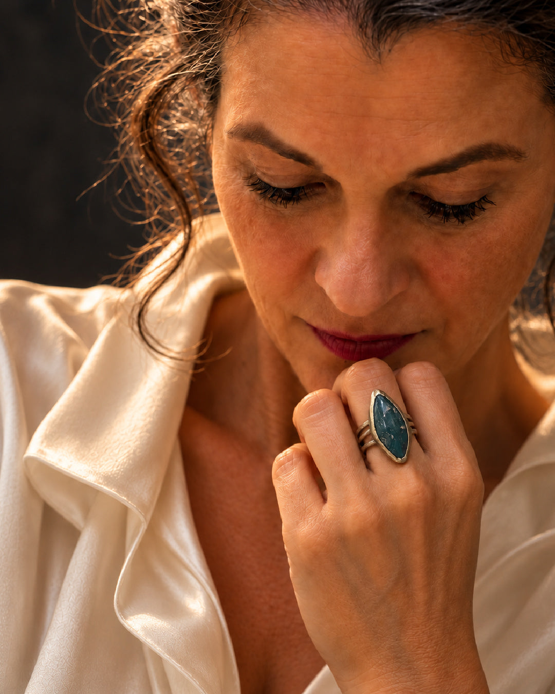 Editorial portrait of a woman in an ivory blouse wearing The Mariposa Ring by Lepa Jewelry, an elongated green mariposite stone in a sculptural brass setting.