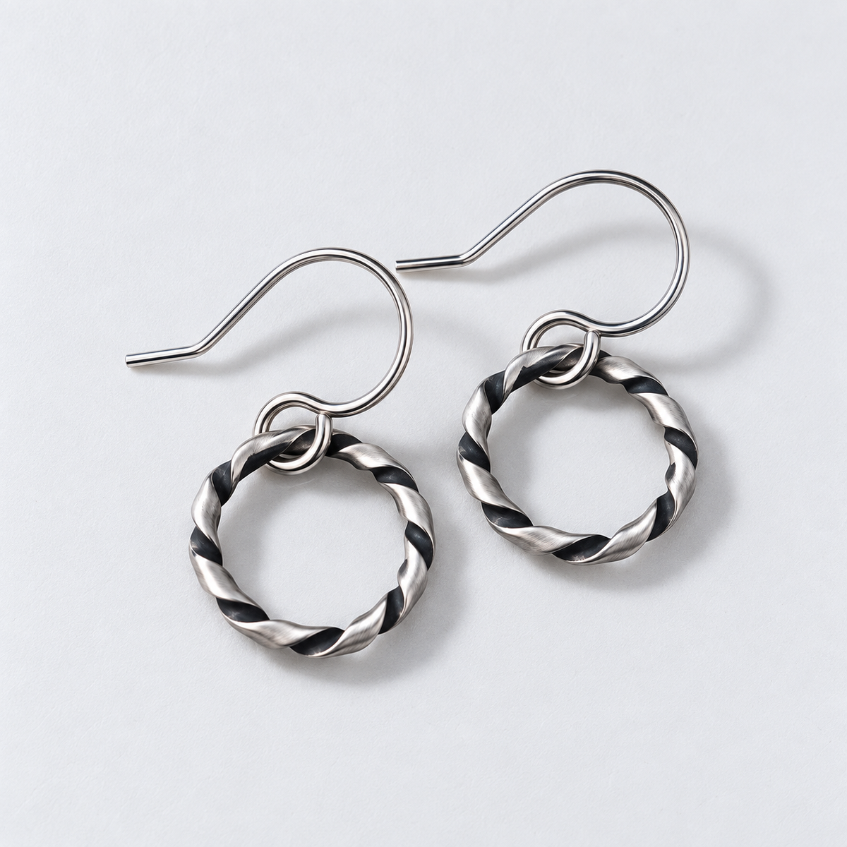 A pair of structural, oxidized argentium silver twisted hoop dangle earrings with fishhook backs, displayed on a white background.