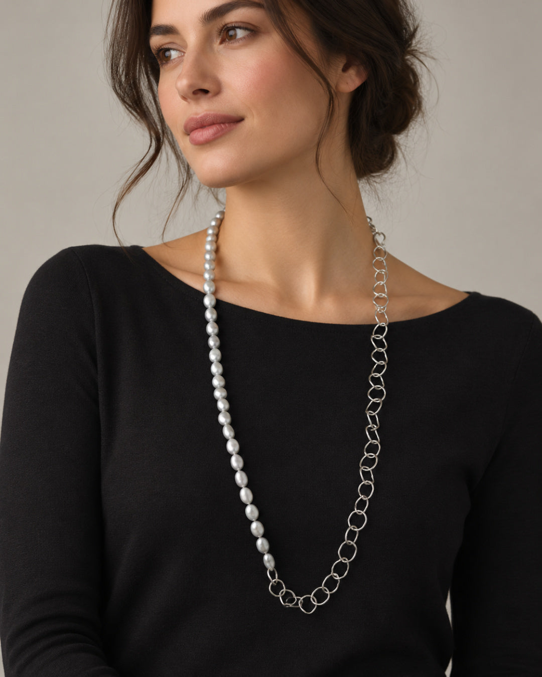 Model wearing the 32-inch Selene Necklace with grey baroque freshwater pearls on one side and sculptural silver links on the other over a black top.