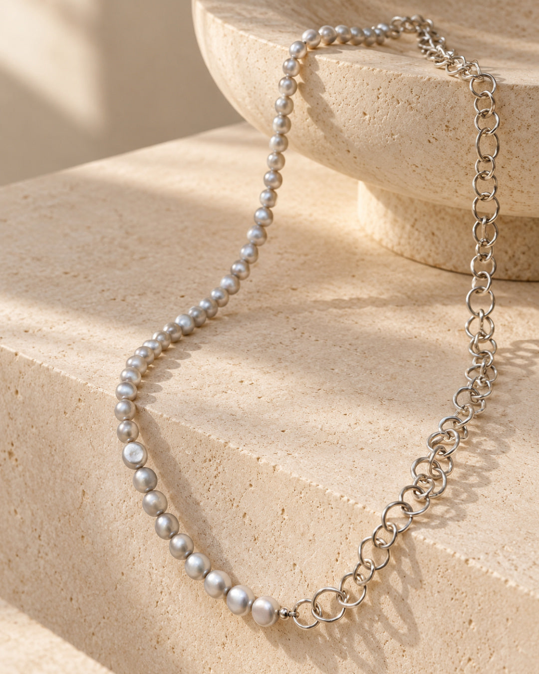 Selene Pearl Necklace featuring pale grey baroque freshwater pearls and sculptural Argentium silver links draped over warm ivory stone