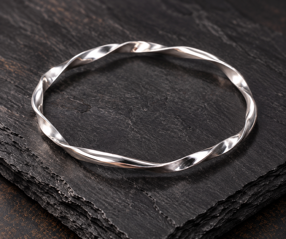 A polished silver twisted bangle bracelet displayed on a dark textured slate surface.