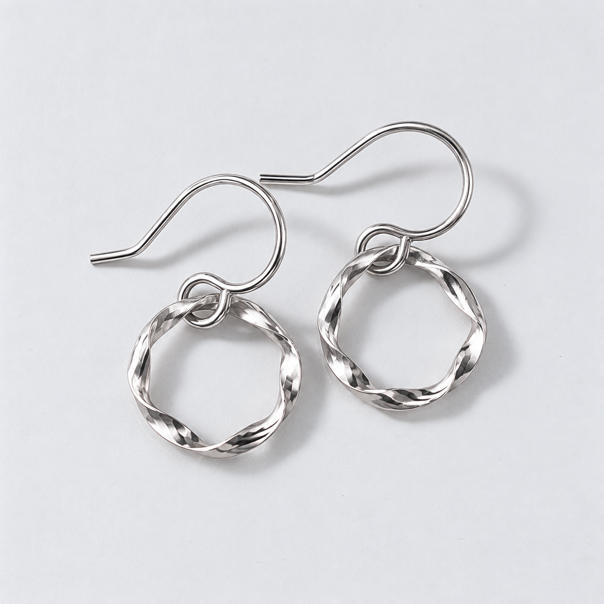 A pair of silver-toned twisted hoop dangle earrings with fishhook wires, displayed on a clean light gray background.