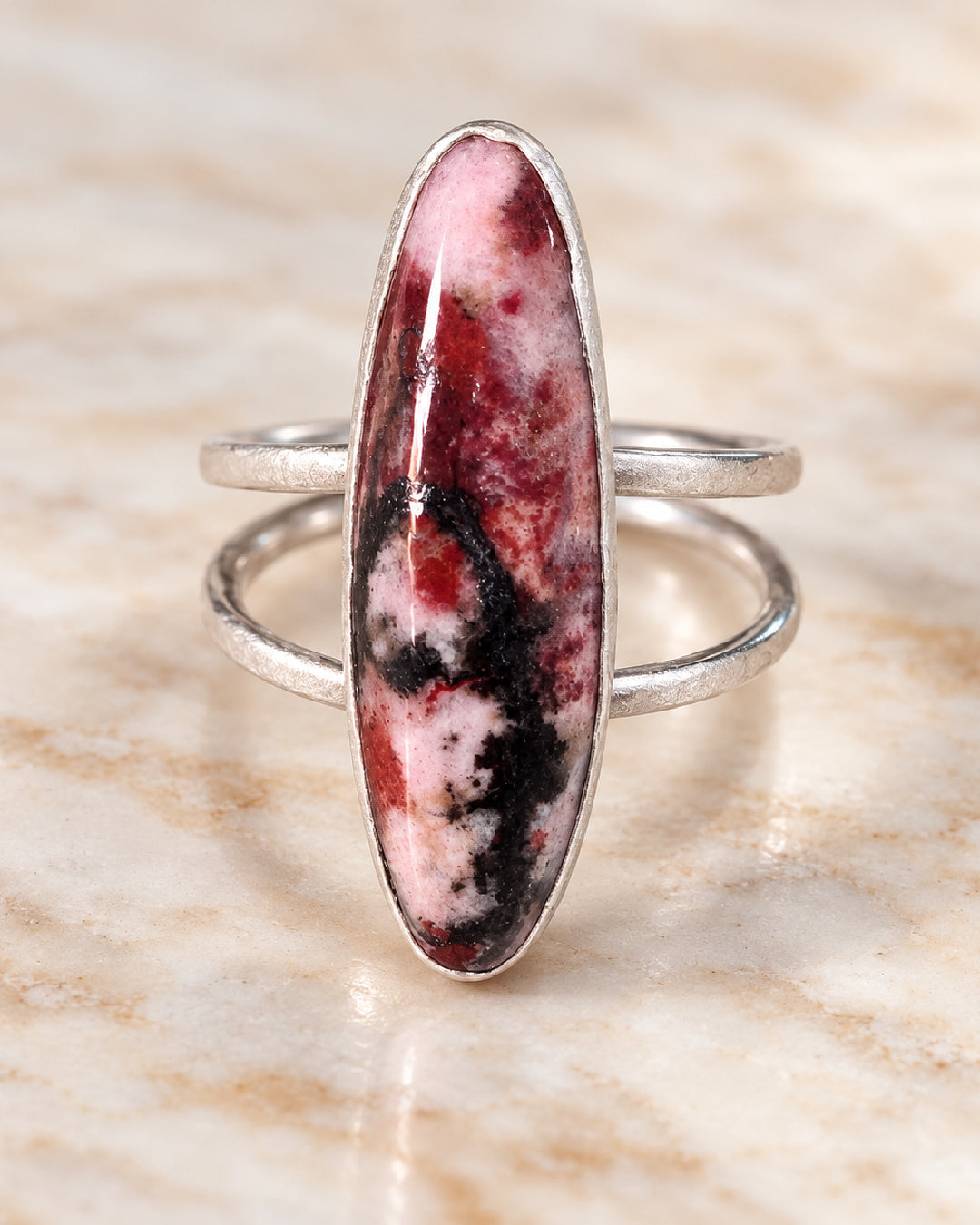 The Sola Ring by Lepa Jewelry featuring an elongated pink, burgundy, and black rhodonite cabochon in a brushed silver bezel with an open split shank.