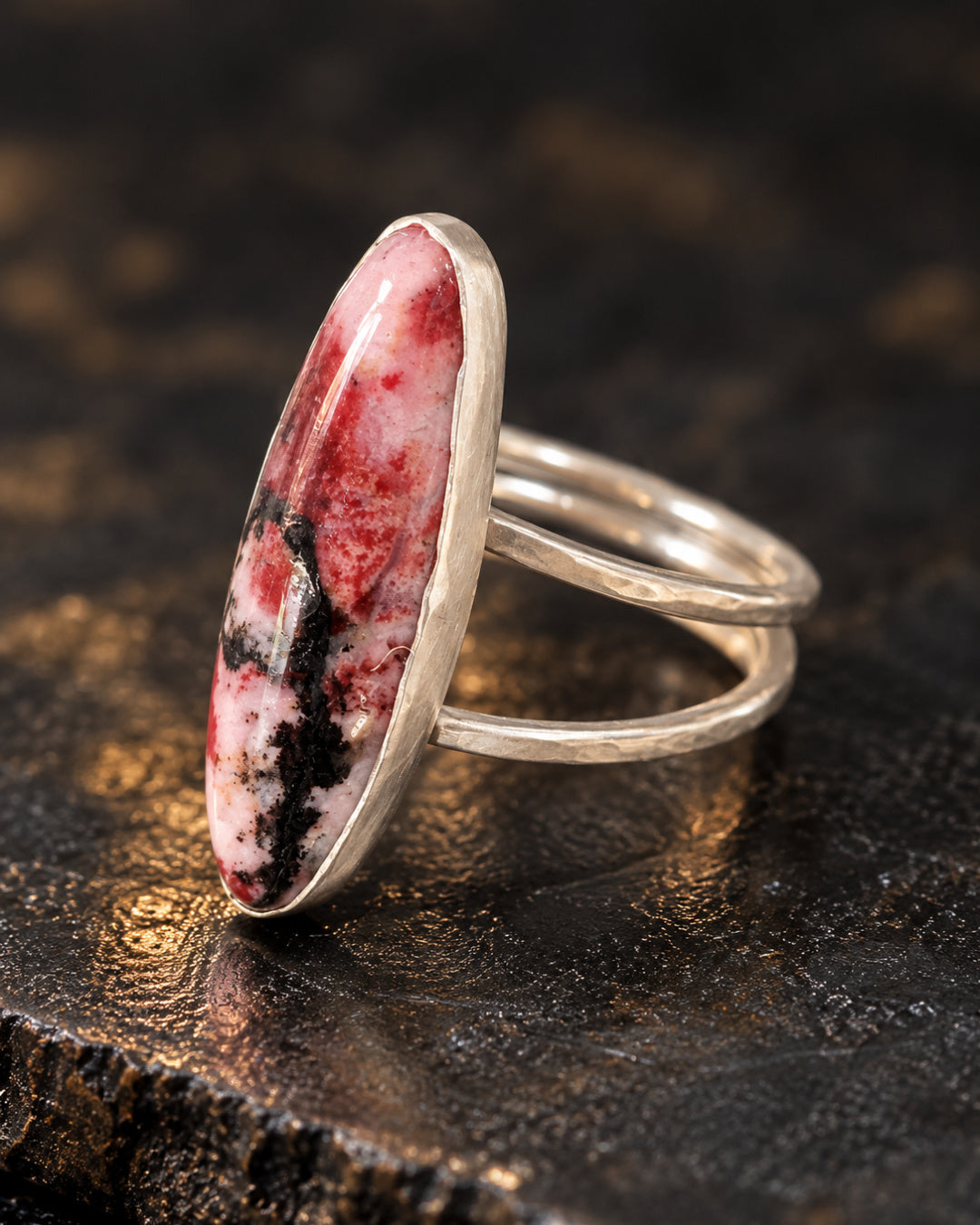 Angled side view of The Sola Ring featuring a polished rhodonite cabochon framed in brushed fine silver and an open, sculptural Argentium silver band.
