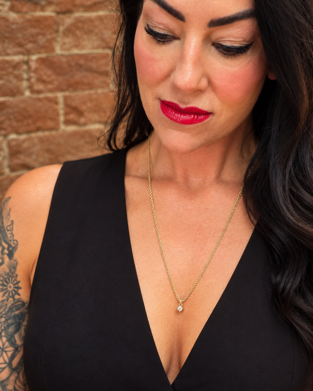 Woman wearing the Lepa Jewelry Sultry Drop Necklace, featuring a delicate CZ pendant on a 24-inch gold-filled chain with a plunging black neckline.