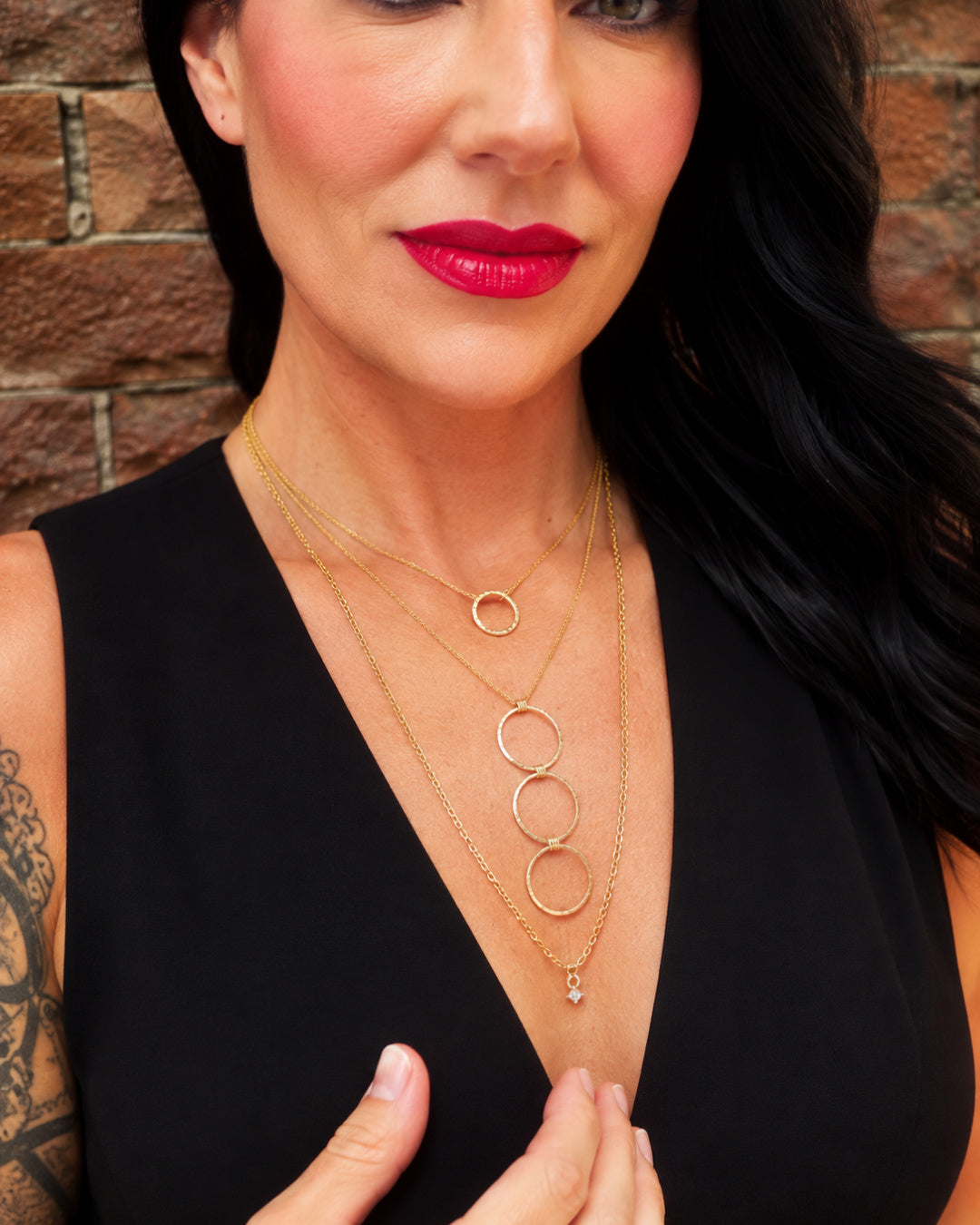 Sultry Drop Necklace layered beneath the Linear Luxe Necklace Day Edition, featuring three sculptural gold-filled circles, worn with a black V-neck top.