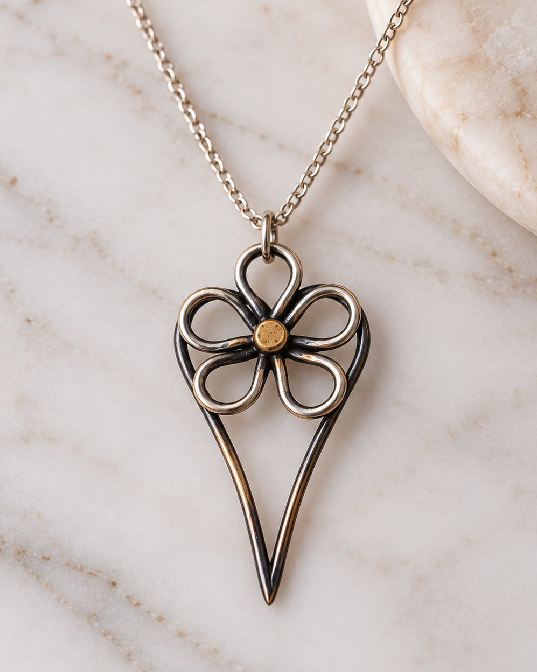 Wild Rose Heart Necklace displayed on a light marble background, highlighting the open floral design, gold-toned center, and elongated oxidized heart pendant.